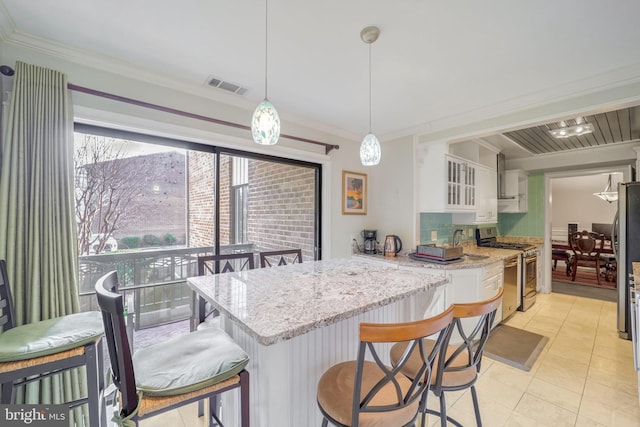 kitchen with a kitchen bar, kitchen peninsula, gas stove, pendant lighting, and white cabinets