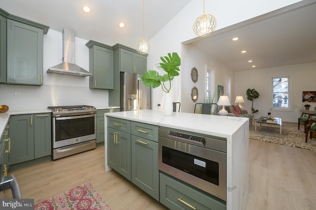 kitchen featuring hanging light fixtures, appliances with stainless steel finishes, green cabinetry, and wall chimney exhaust hood