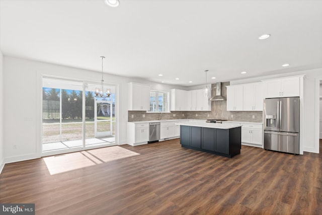 kitchen with white cabinets, stainless steel appliances, hanging light fixtures, and wall chimney range hood