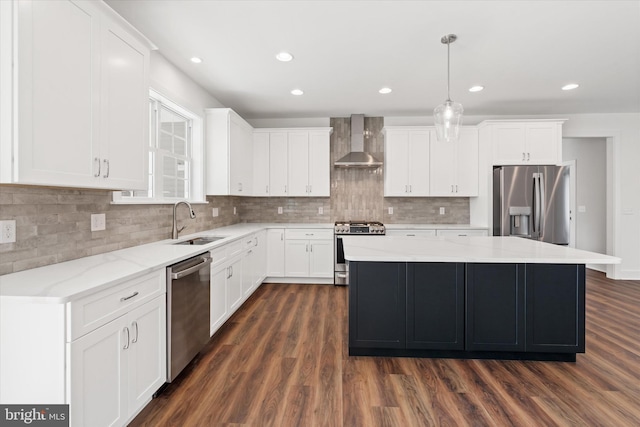 kitchen with wall chimney range hood, sink, appliances with stainless steel finishes, decorative light fixtures, and a kitchen island