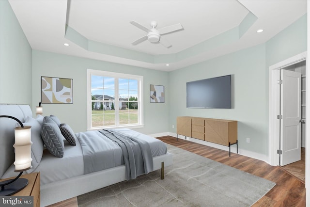 bedroom with hardwood / wood-style floors, ceiling fan, and a raised ceiling