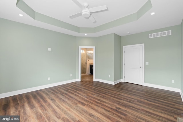 unfurnished bedroom featuring ceiling fan, dark wood-type flooring, connected bathroom, and a tray ceiling