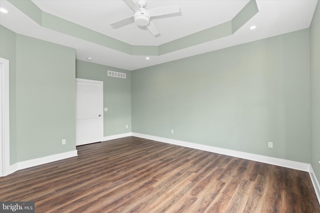 empty room featuring dark hardwood / wood-style flooring, a raised ceiling, and ceiling fan