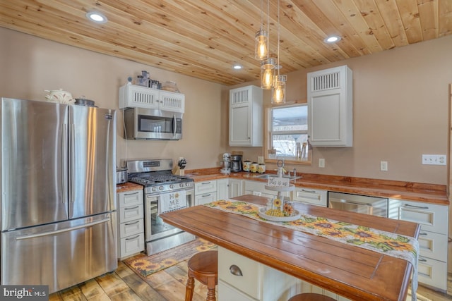 kitchen with wooden counters, appliances with stainless steel finishes, decorative light fixtures, and white cabinetry