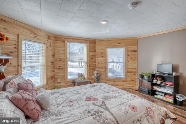 bedroom featuring hardwood / wood-style flooring, wood walls, and multiple windows