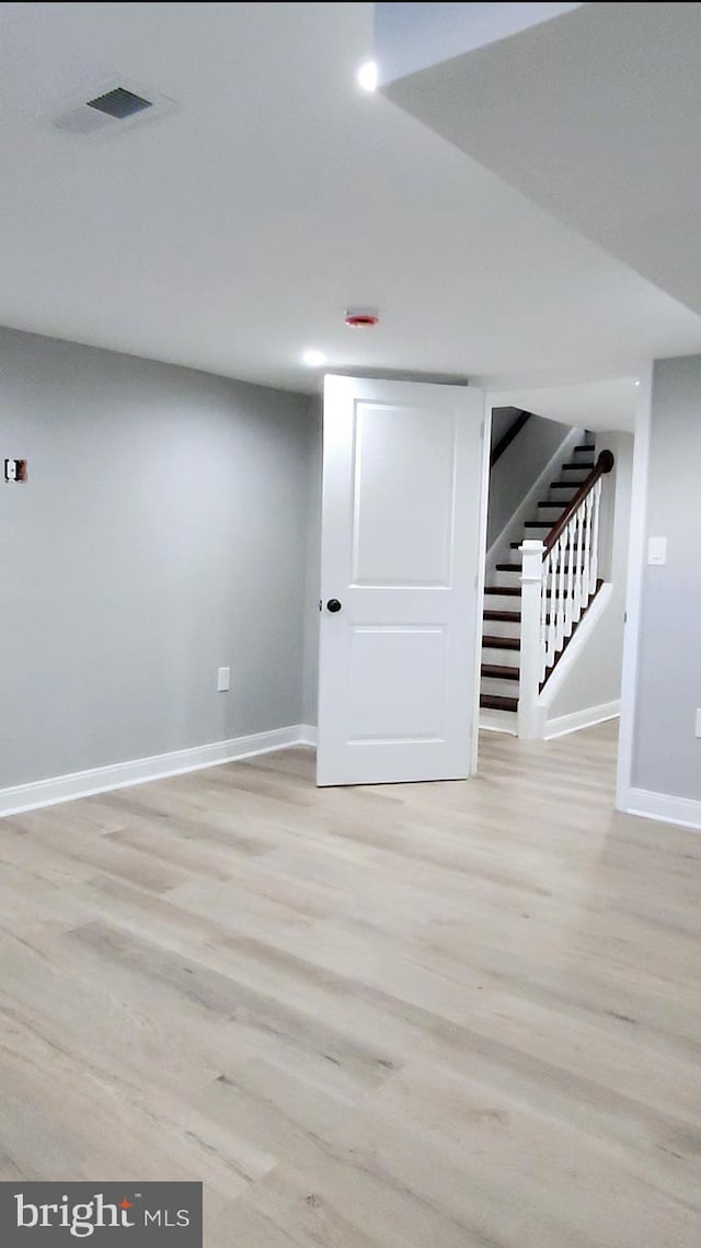 below grade area with light wood-style flooring, stairs, baseboards, and visible vents