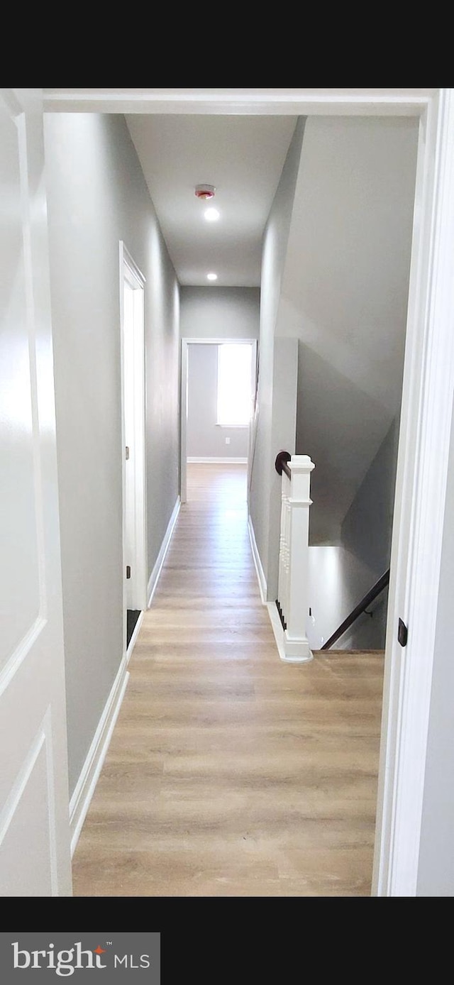 hall featuring baseboards, wood finished floors, and an upstairs landing