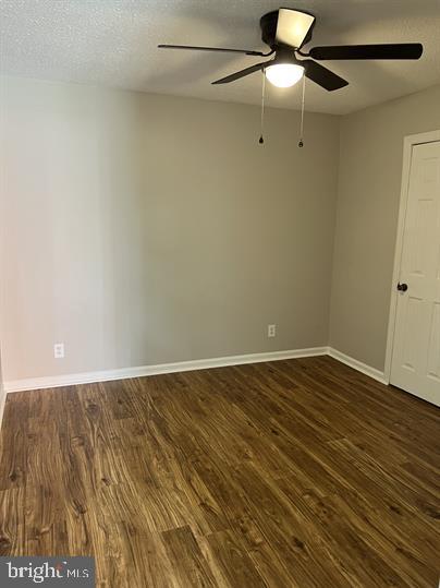 spare room with a textured ceiling, ceiling fan, and dark wood-type flooring