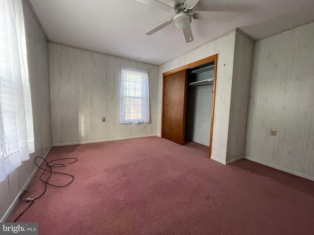 unfurnished bedroom featuring ceiling fan, wood walls, light carpet, and a closet