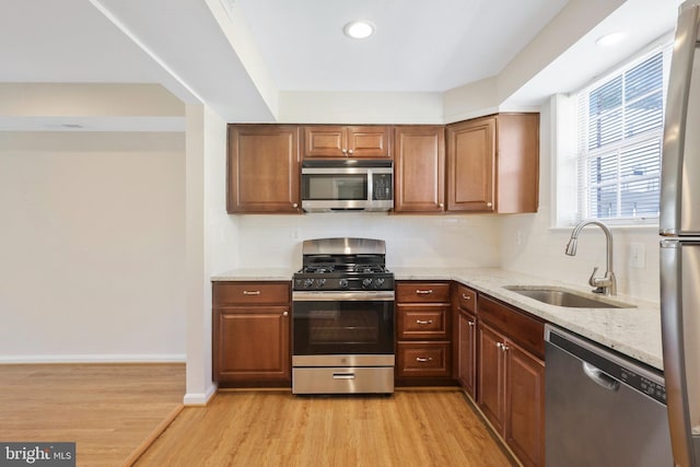 kitchen with appliances with stainless steel finishes, light wood-type flooring, light stone counters, and sink