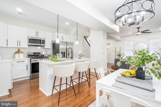 kitchen with white cabinets, appliances with stainless steel finishes, ceiling fan with notable chandelier, and hanging light fixtures