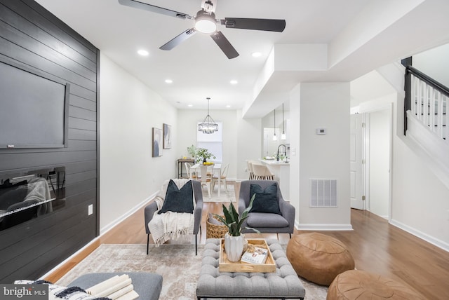 living room with sink, light hardwood / wood-style floors, and ceiling fan with notable chandelier