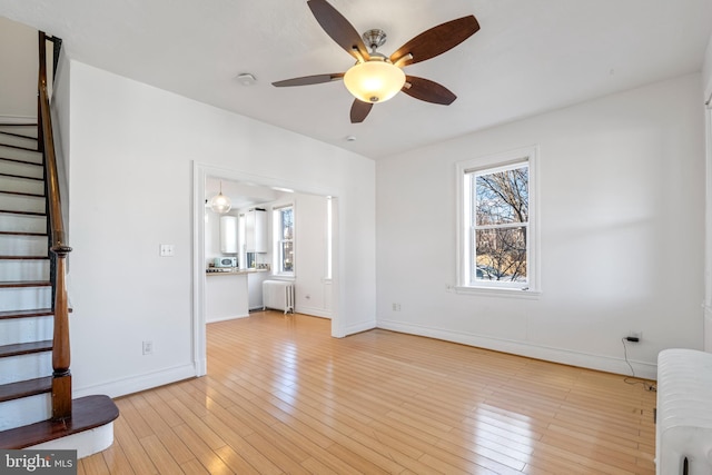 unfurnished living room with ceiling fan, radiator heating unit, and light hardwood / wood-style flooring