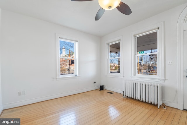 unfurnished room with ceiling fan, radiator heating unit, and light wood-type flooring