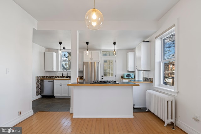 kitchen featuring pendant lighting, radiator heating unit, white cabinetry, kitchen peninsula, and stainless steel appliances