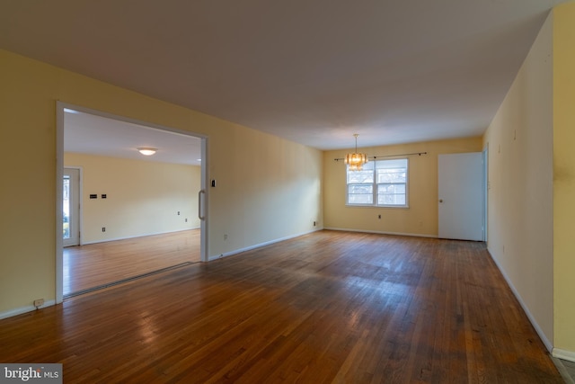 empty room with dark wood-type flooring and an inviting chandelier