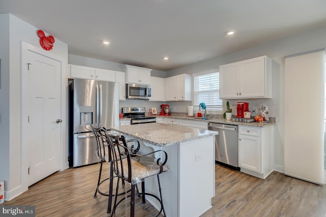 kitchen featuring light wood-type flooring, stainless steel appliances, white cabinetry, a kitchen island, and a breakfast bar area