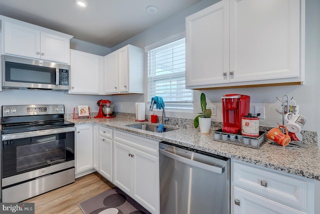 kitchen featuring appliances with stainless steel finishes, light stone counters, sink, light hardwood / wood-style flooring, and white cabinets