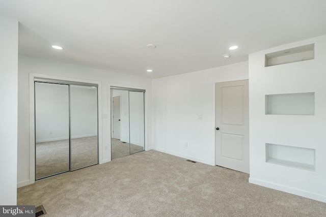 unfurnished bedroom with light colored carpet and multiple closets