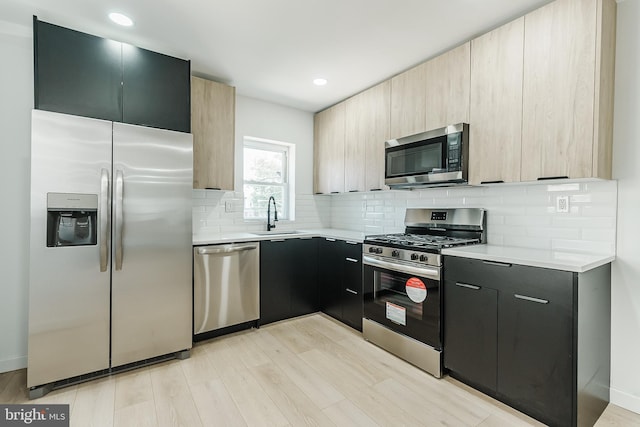 kitchen with appliances with stainless steel finishes, light brown cabinetry, tasteful backsplash, sink, and light hardwood / wood-style flooring