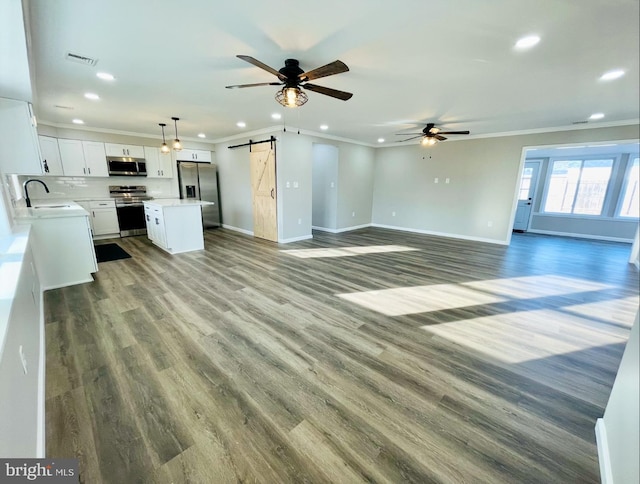 unfurnished living room featuring sink, hardwood / wood-style flooring, ceiling fan, a barn door, and ornamental molding