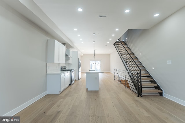 kitchen featuring white cabinets, decorative light fixtures, an island with sink, and appliances with stainless steel finishes