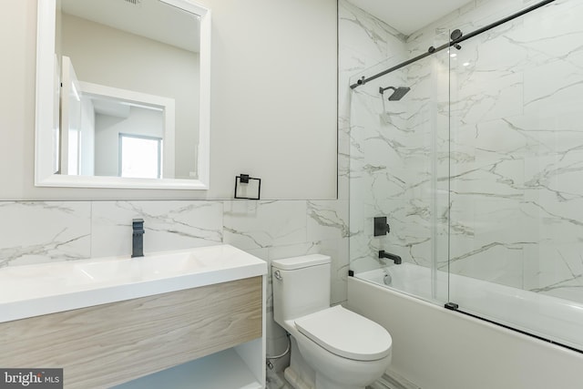 full bathroom featuring vanity, toilet, bath / shower combo with glass door, and tile walls