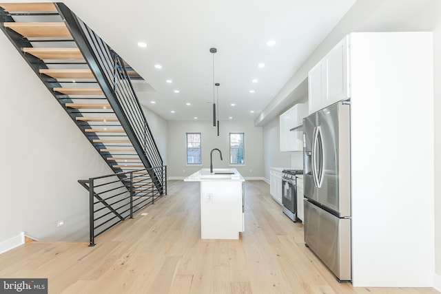 kitchen featuring pendant lighting, light hardwood / wood-style flooring, an island with sink, appliances with stainless steel finishes, and white cabinetry