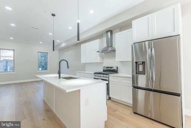 kitchen with appliances with stainless steel finishes, wall chimney exhaust hood, a kitchen island with sink, sink, and hanging light fixtures