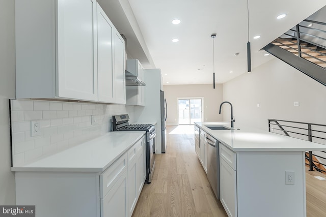 kitchen with appliances with stainless steel finishes, a kitchen island with sink, sink, white cabinets, and hanging light fixtures