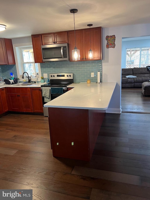 kitchen featuring tasteful backsplash, dark hardwood / wood-style floors, kitchen peninsula, pendant lighting, and appliances with stainless steel finishes