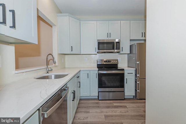 kitchen featuring sink, stainless steel appliances, light stone counters, light hardwood / wood-style flooring, and white cabinets