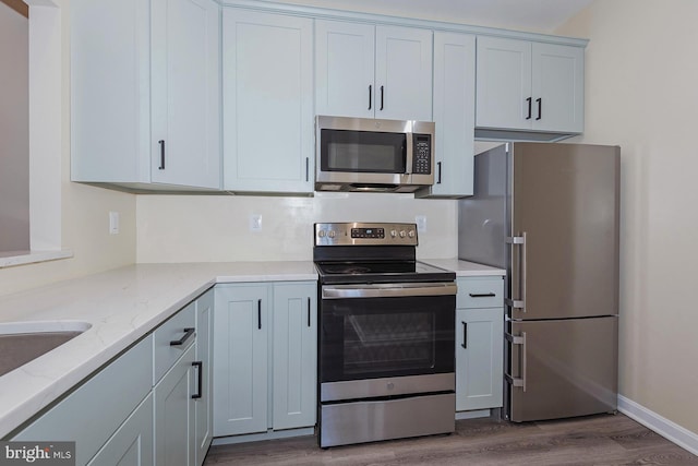 kitchen featuring light stone countertops, wood-type flooring, sink, and appliances with stainless steel finishes