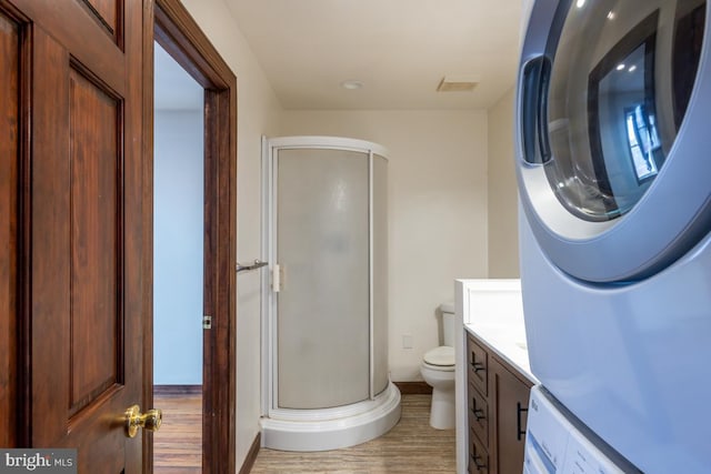 bathroom with stacked washer / dryer, vanity, an enclosed shower, wood-type flooring, and toilet