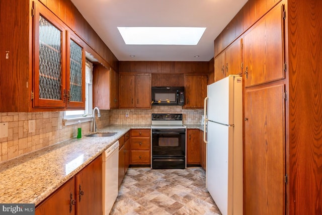 kitchen featuring sink, white appliances, backsplash, a skylight, and light stone counters