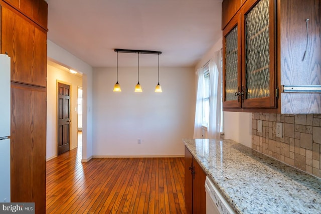 kitchen featuring tasteful backsplash, decorative light fixtures, white refrigerator, hardwood / wood-style flooring, and light stone countertops