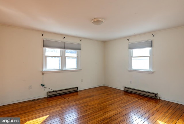 empty room with a wealth of natural light, a baseboard heating unit, and hardwood / wood-style floors