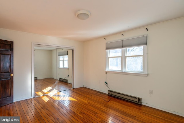 unfurnished bedroom with a baseboard radiator, wood-type flooring, and a closet