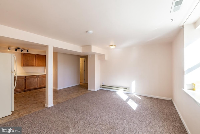 basement with track lighting, light colored carpet, baseboard heating, and white refrigerator