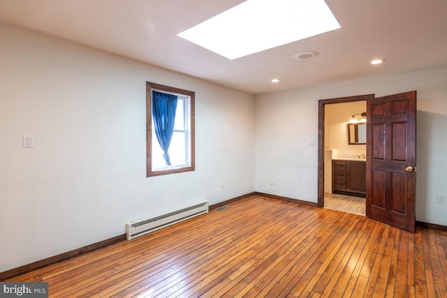 unfurnished bedroom with a skylight, a baseboard heating unit, ensuite bath, and light hardwood / wood-style flooring