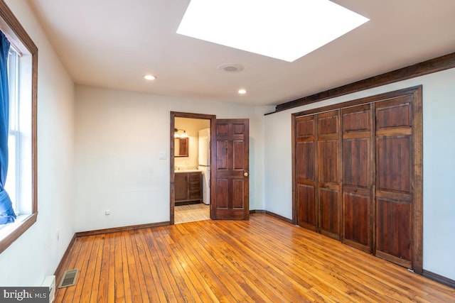 unfurnished bedroom with light hardwood / wood-style flooring, connected bathroom, a skylight, and a closet