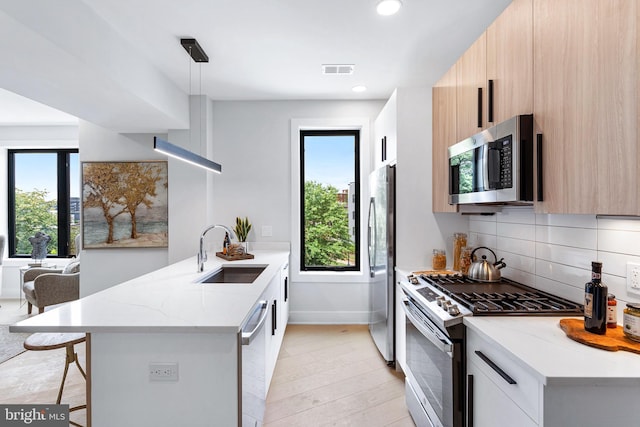 kitchen featuring sink, hanging light fixtures, light stone countertops, kitchen peninsula, and stainless steel appliances