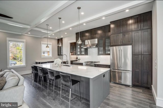 kitchen with ventilation hood, a center island with sink, sink, decorative light fixtures, and high end fridge