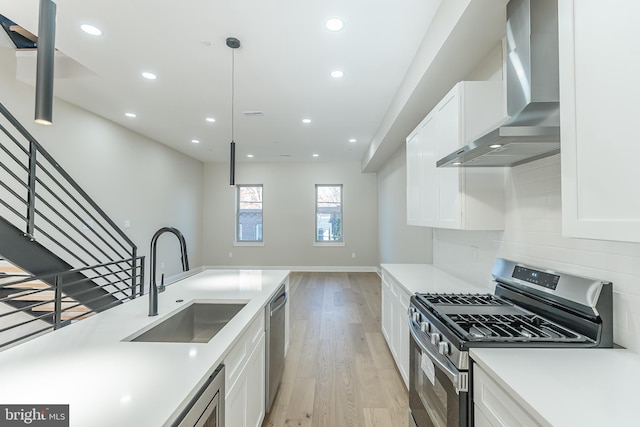 kitchen featuring sink, wall chimney range hood, decorative light fixtures, white cabinets, and appliances with stainless steel finishes