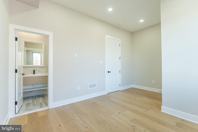 unfurnished bedroom featuring ensuite bathroom and light hardwood / wood-style flooring