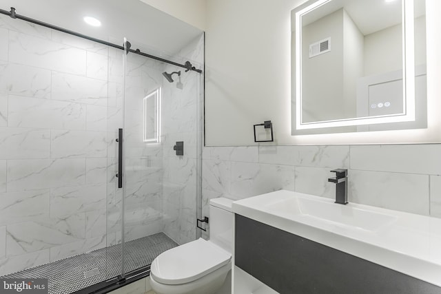 bathroom with vanity, toilet, tile walls, and a shower with shower door