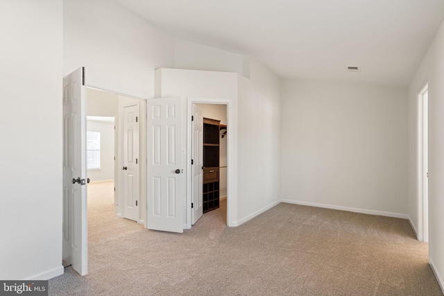 unfurnished bedroom with lofted ceiling, a walk in closet, and light carpet