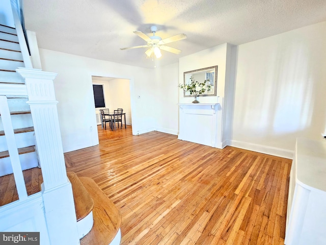 living room featuring ceiling fan, a textured ceiling, and light wood-type flooring