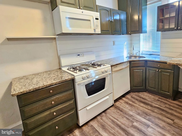 kitchen with dark brown cabinetry, light stone counters, sink, and white appliances