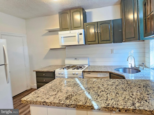 kitchen featuring sink, dark wood-type flooring, light stone counters, a textured ceiling, and white appliances